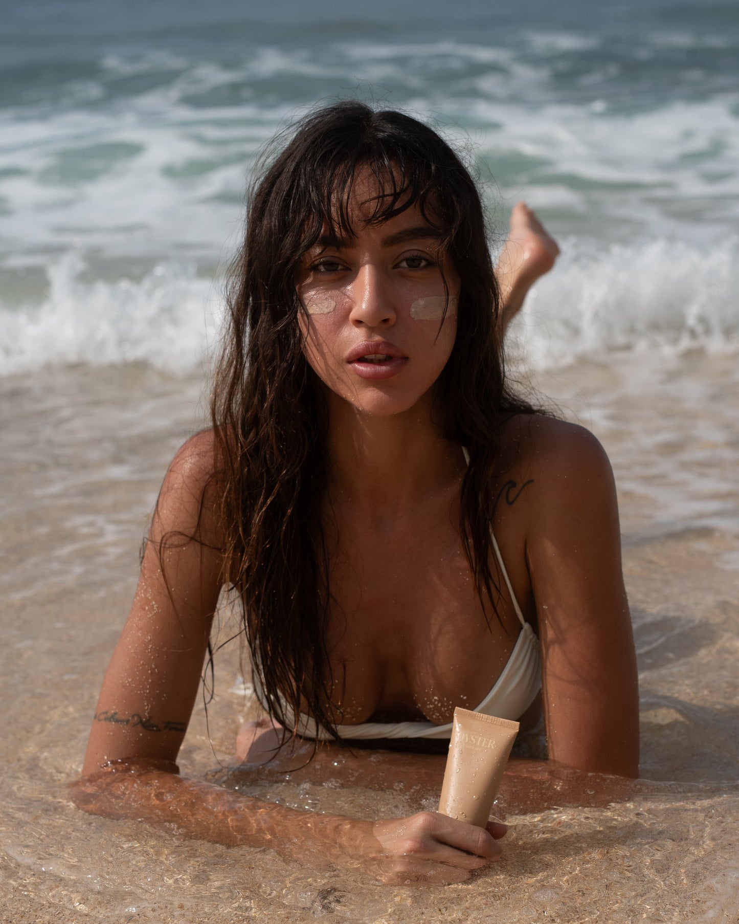 Woman lying in shallow water at the beach with ocean waves in the background